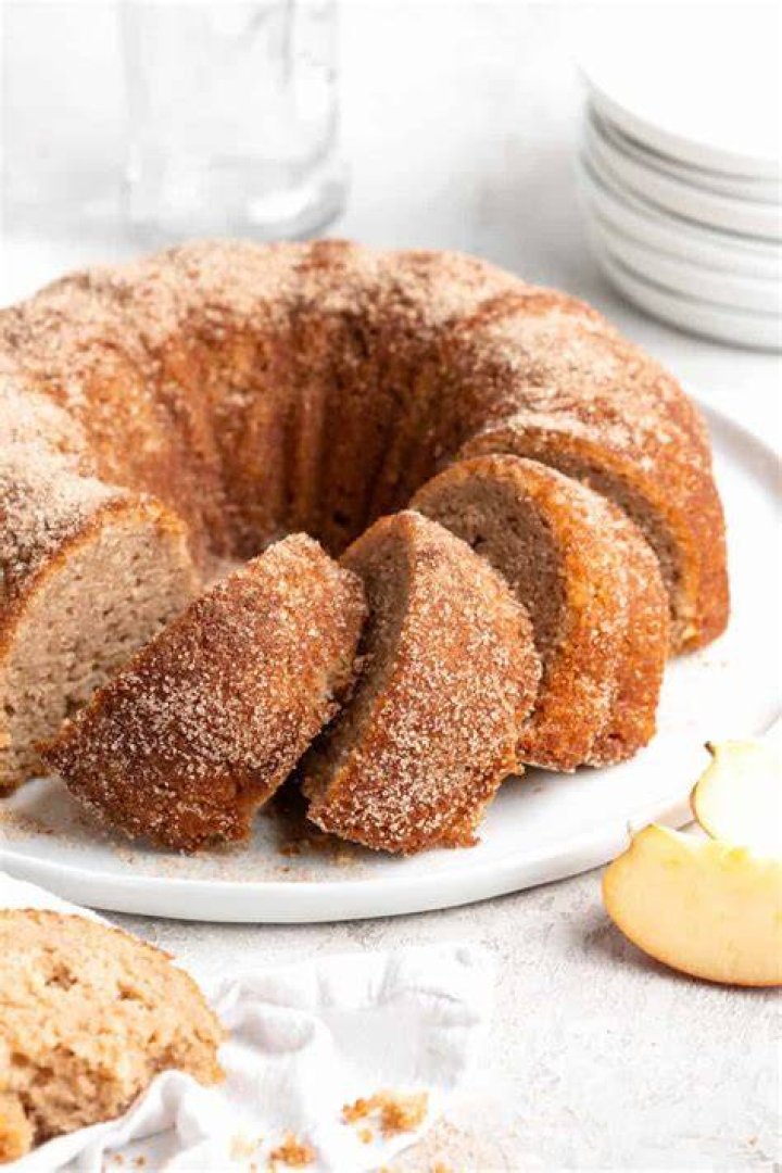 Apple Cider Donut Cake covered in cinnamon sugar on a round white plate.
