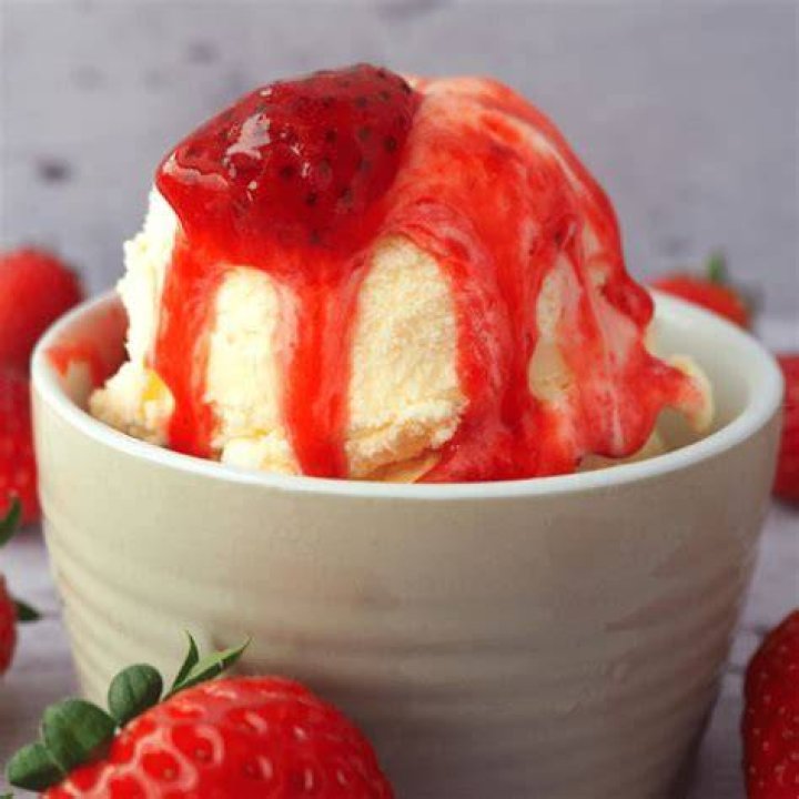 Strawberry sauce on ice cream in a white bowl with a gold spoon.
